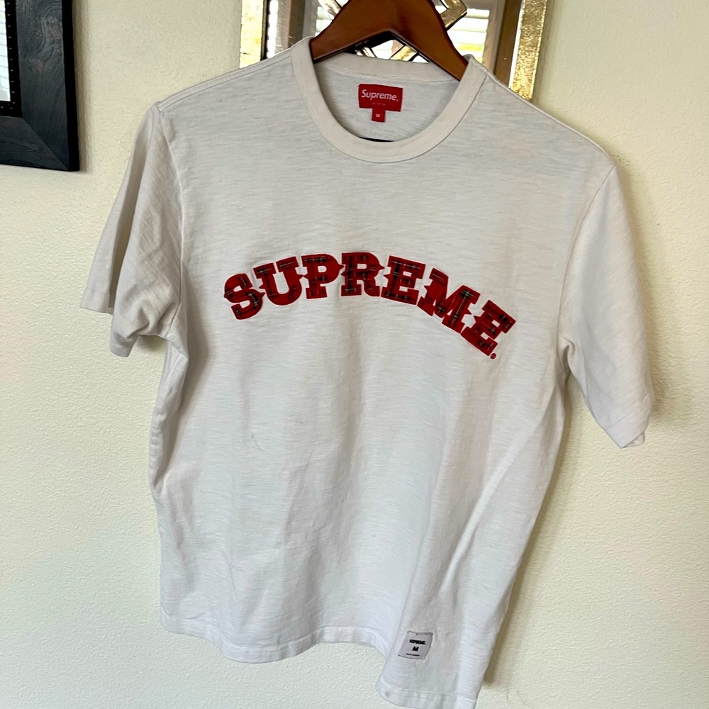 Supreme tshirt with logo on front in red plaid writing.